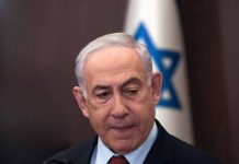 Man in suit with Israeli flag in background.