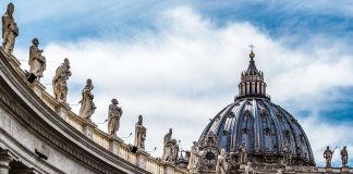 St. Peter's Basilica dome with statues and clouds.