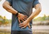 Person holding lower back in discomfort outdoors