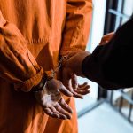 Handcuffed person in orange jumpsuit being escorted