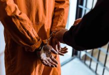 Handcuffed person in orange jumpsuit being escorted