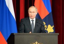 Man speaking at podium with flags behind him