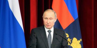 Man speaking at podium with flags behind him