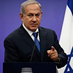 Man speaking at podium with Israeli flag behind him