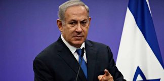 Man speaking at podium with Israeli flag behind him