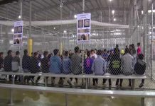 People sitting on benches inside a fenced facility