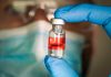 Gloved hand holding vial with red liquid and flag