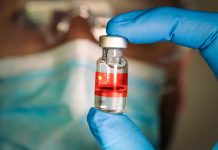 Gloved hand holding vial with red liquid and flag