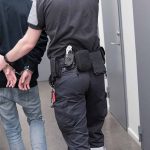 Officer escorting handcuffed person down hallway