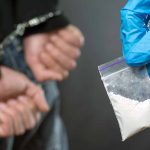 Handcuffed person with small bag of white marijuana