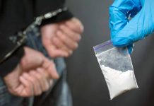 Handcuffed person with small bag of white marijuana