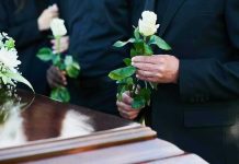 Mourners holding white roses by a casket