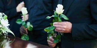 Mourners holding white roses by a casket