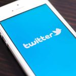 Close up of a smartphone displaying the Twitter logo on a blue background