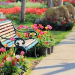 A decorative garden bench surrounded by vibrant flowers in a park