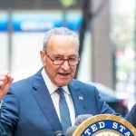 Man in suit and glasses speaks passionately at podium.