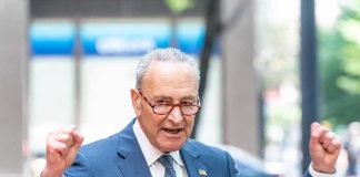 Man in suit and glasses speaks passionately at podium.