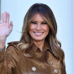 Person smiling and waving wearing a brown coat