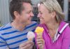 Couple smiling with ice cream cones outside bench