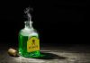 Green poison bottle with cork on wooden surface.