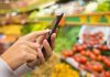 Person using a smartphone while shopping for fresh produce in a grocery store