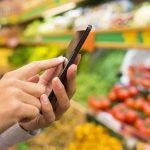Person using a smartphone while shopping for fresh produce in a grocery store