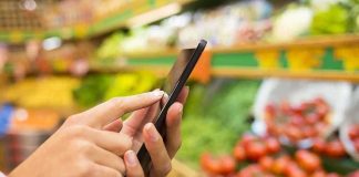 Person using a smartphone while shopping for fresh produce in a grocery store