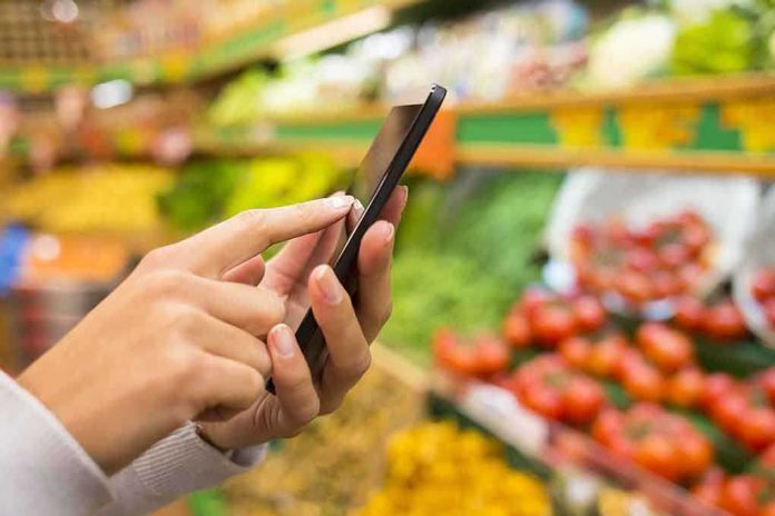 Person using a smartphone while shopping for fresh produce in a grocery store