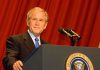 A man in a suit standing at a podium with microphones and a presidential seal