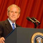 A man in a suit standing at a podium with microphones and a presidential seal