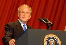 A man in a suit standing at a podium with microphones and a presidential seal
