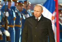 Man in black coat with soldiers in background.