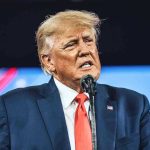 Trump WIPES Student Debt – Biden 2.0? Man in suit speaking at a microphone.