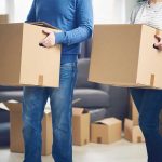 Exodus EXPOSED — Blue States Bleed Families Two people carrying cardboard boxes indoors.