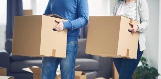 Exodus EXPOSED — Blue States Bleed Families Two people carrying cardboard boxes indoors.