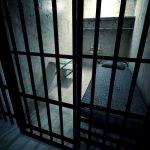 Interior view of a prison cell with a bed and metal bars