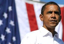 A man in a white shirt standing in front of an American flag