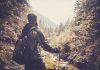A hiker standing in a forest, looking at a scenic view of mountains and trees