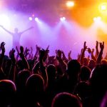 Pop Star EXPLODES – Profanity-Laced ICE Tirade! Crowd at a concert with raised hands and colorful stage lights