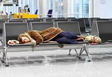 A traveler sleeping on a bench in an airport waiting area