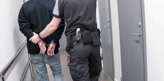 Escaped Predator CAUGHT – He Was Where? Officer escorting handcuffed person down hallway.