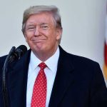 Tariff Check CHAOS—$2,000 Windfall or Epic Flop? Man in suit and tie speaking at podium.