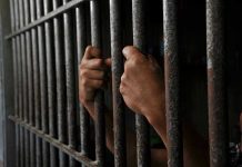 Prison MASSACRE Kills 35 – Suffocation Deaths Exposed Hands gripping prison cell bars tightly.