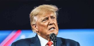 Congressional Revolt Triggers TRUMP CRISIS Mode Man in suit speaking at a microphone.