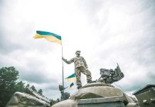 Soldier on tank holding Ukrainian flag.