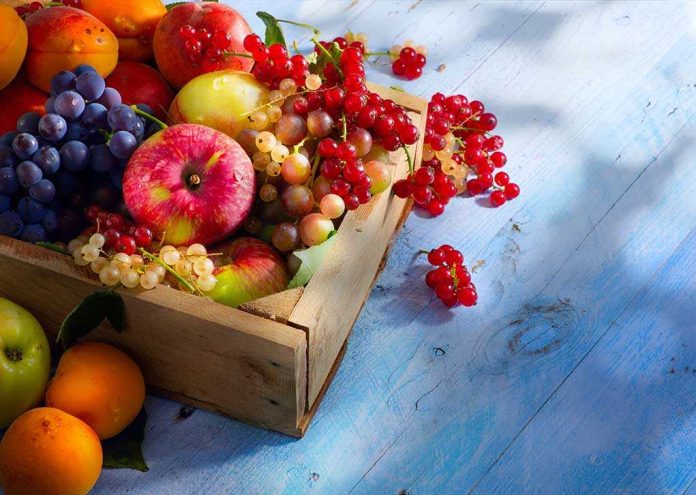 A wooden crate filled with a variety of fresh fruits including apples grapes and berries