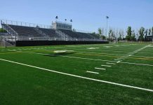 Legendary Coach SHOT – Campus ATTACK Rocks Football World! A football field with artificial turf and empty bleachers under a clear blue sky