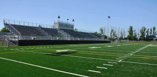 Legendary Coach SHOT – Campus ATTACK Rocks Football World! A football field with artificial turf and empty bleachers under a clear blue sky