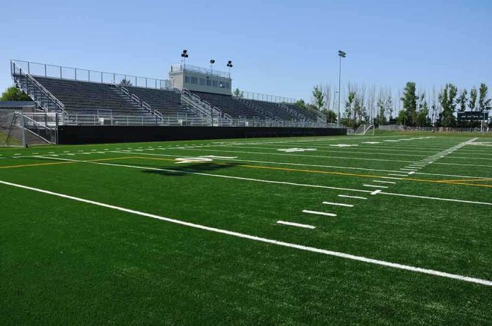 shutterstock_55132081.jpg A football field with artificial turf and empty bleachers under a clear blue sky
