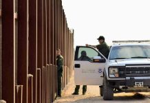 Border patrol agents near a tall metal fence.